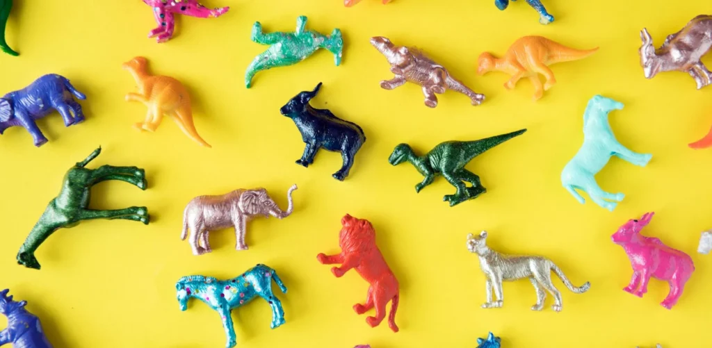 Colourful metallic toy animals and dinosaurs arranged on a yellow background