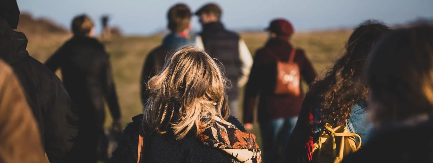 Group of friends walking through open countryside, seen from behind in warm light