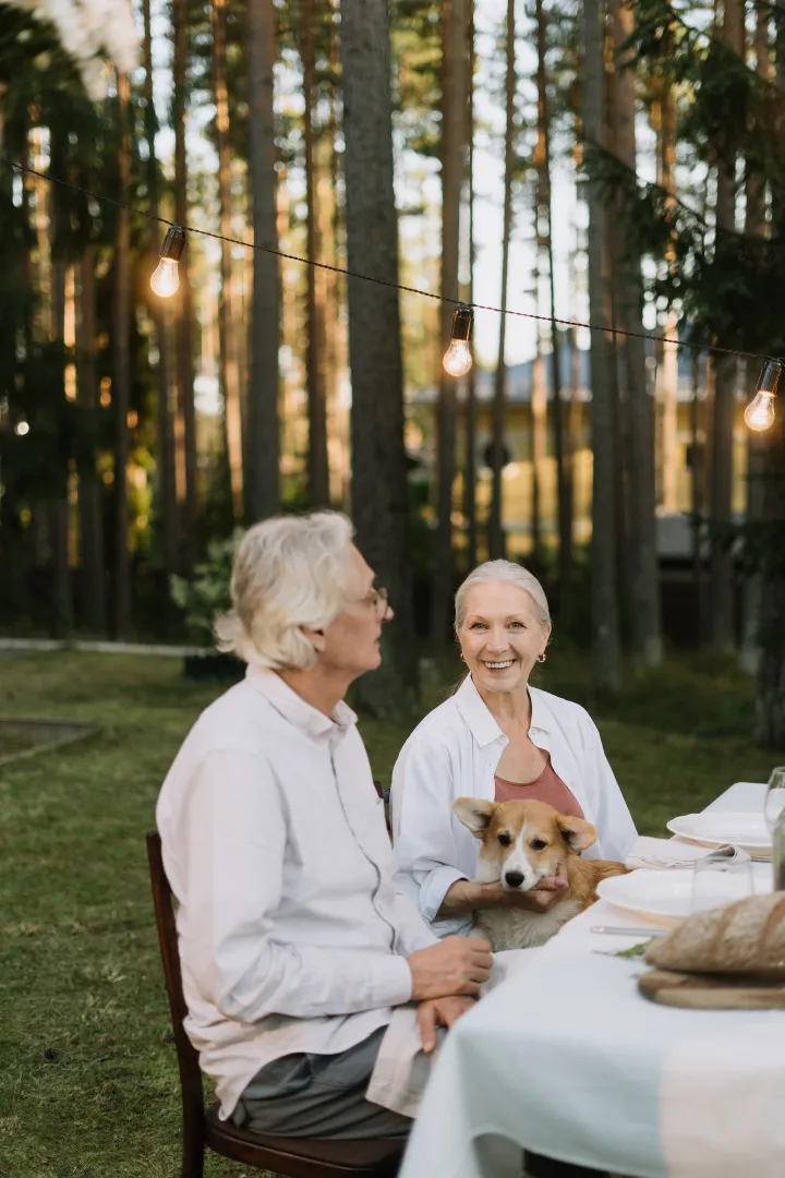 Older couple sitting at an outdoor dinner table with a corgi under string lights