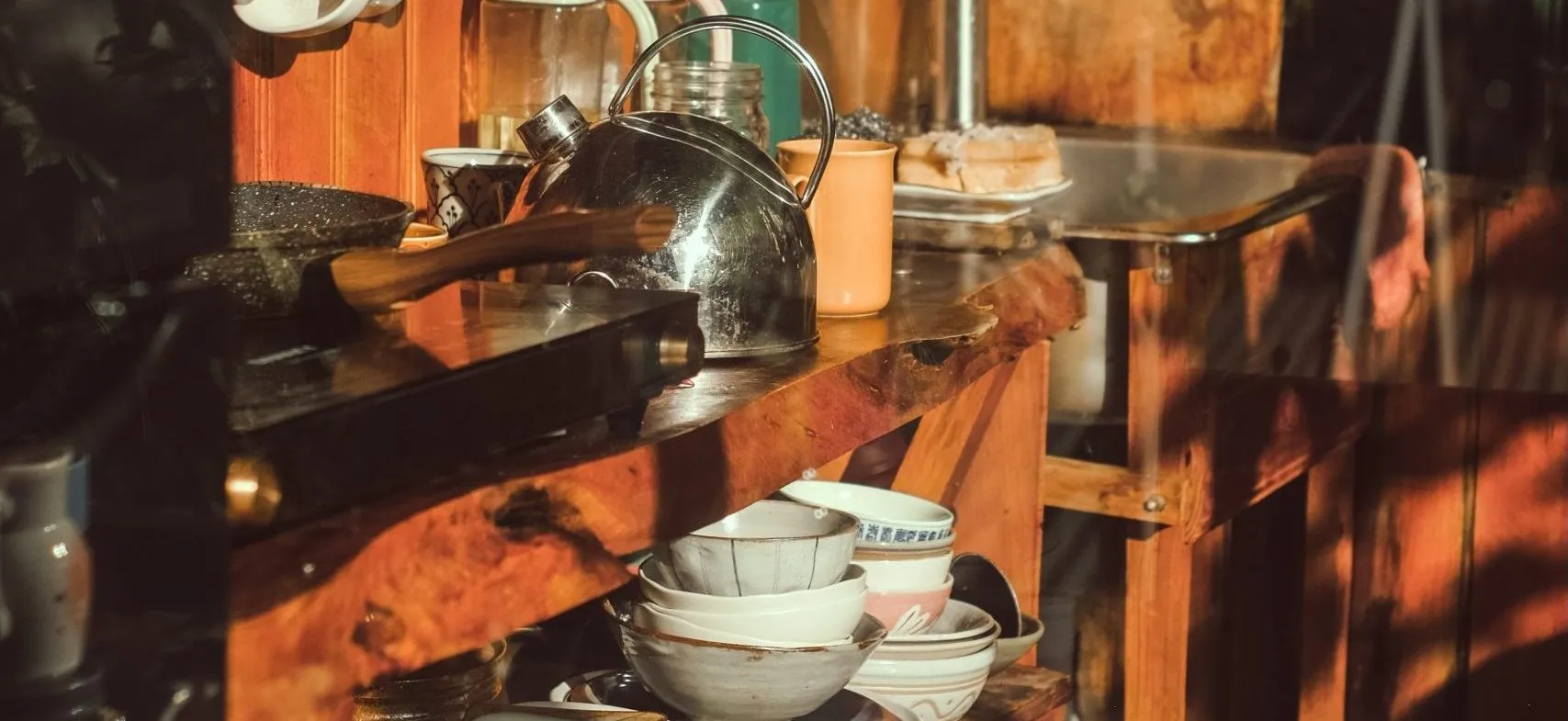 Rustic kitchen shelves with a stainless steel kettle, stacked ceramic bowls and mugs