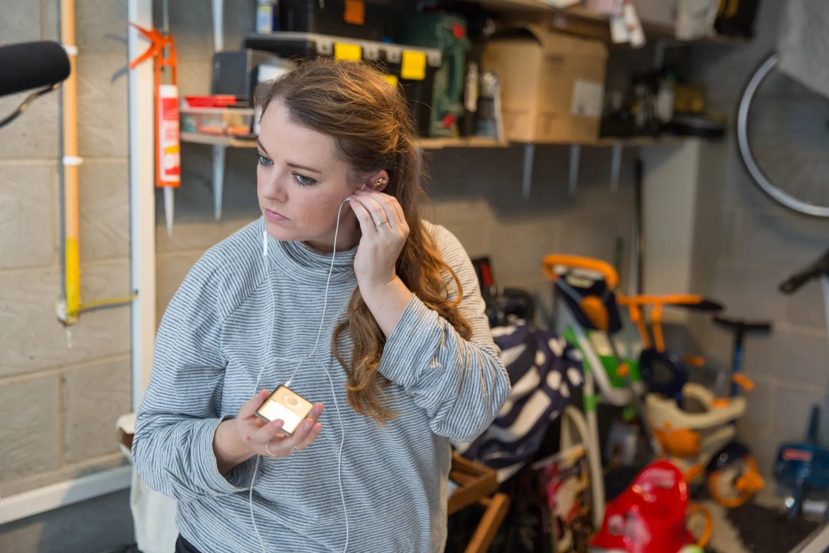 Woman putting in earphones in her garage, holding a music player