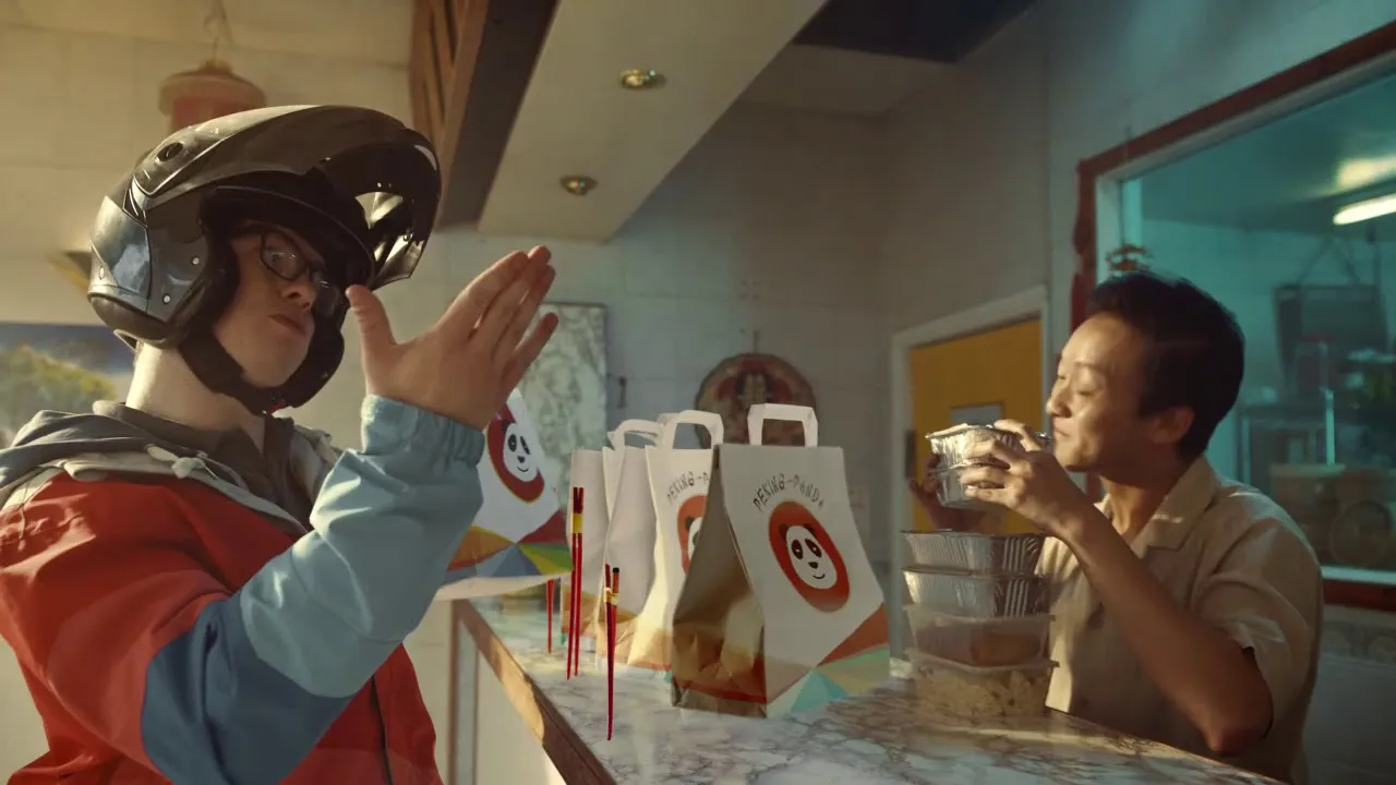 Just Eat courier greeting a Chinese takeaway owner at the counter in a TV advert still
